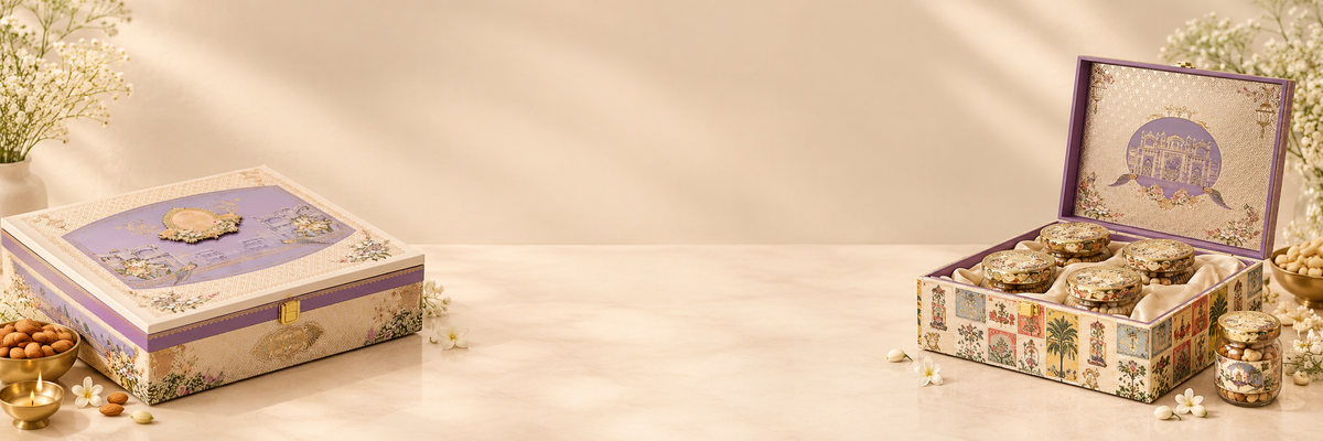 Two decorative gift boxes containing assorted cookies or sweets, styled on a warm beige surface with soft sunlight and floral props. One box is closed in lavender tones, and the other is open showing the illustrated interior lid.
